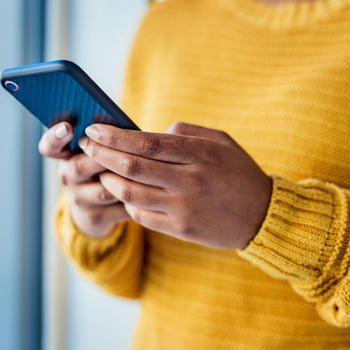 A shot of a woman's hands texting on a blue phone and she's wearing a yellow sweater